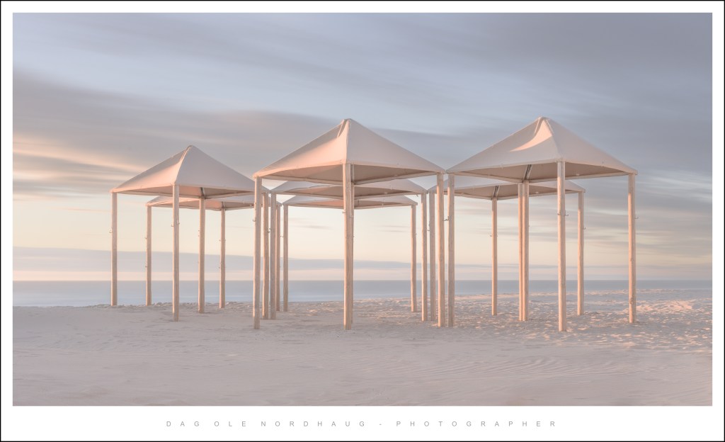 Three white beach cabanas on a sandy shore under a pastel sky.