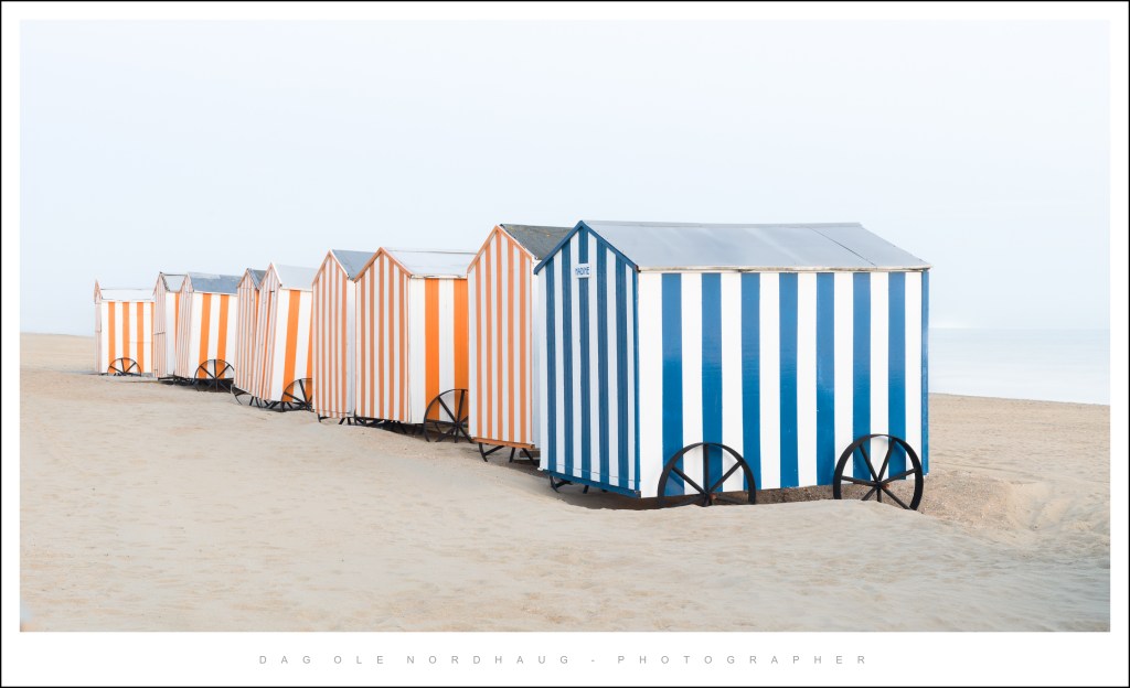 A row of colorful beach huts with blue and orange stripes on sandy beach, creating a scenic coastal view.